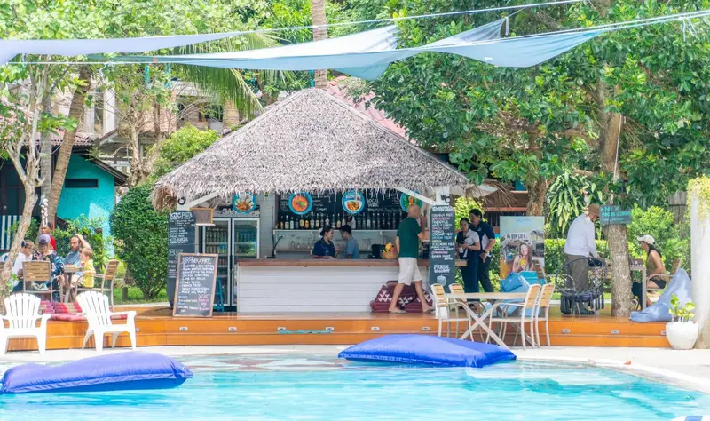 Terrasse ombragée avec un bar et des transats près d'une piscine.