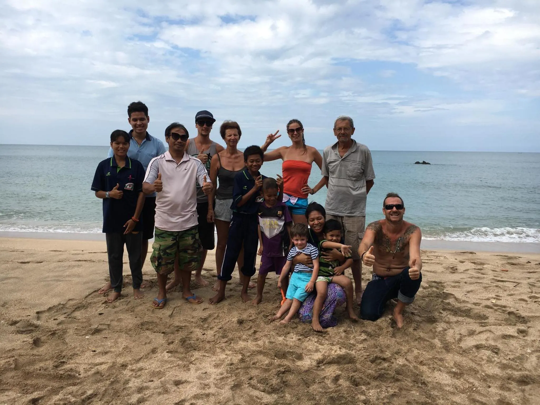 Groupe de personnes souriantes posant sur une plage de sable fin face à la mer.