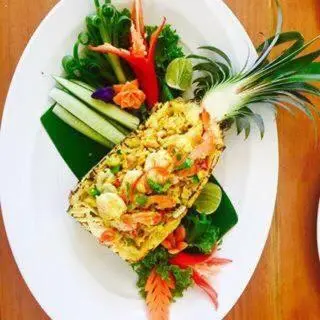 Un plat de riz frit servi dans un ananas, décoré de légumes et de fruits.