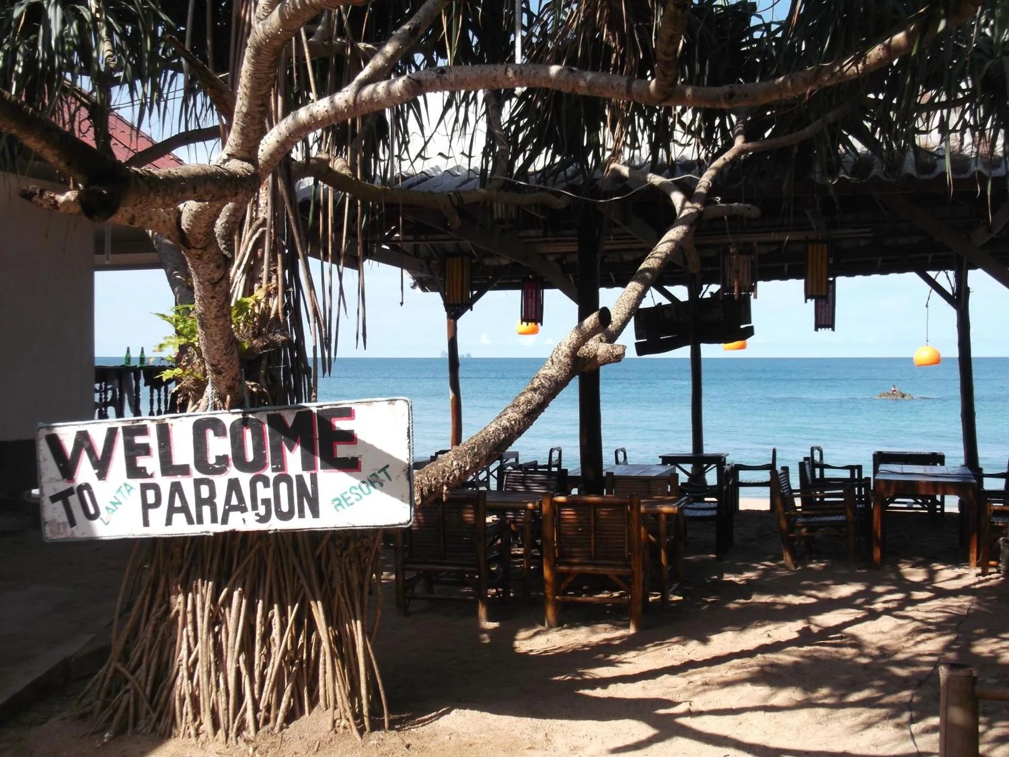 Terrasse ombragée donnant sur la mer et une plage de sable.