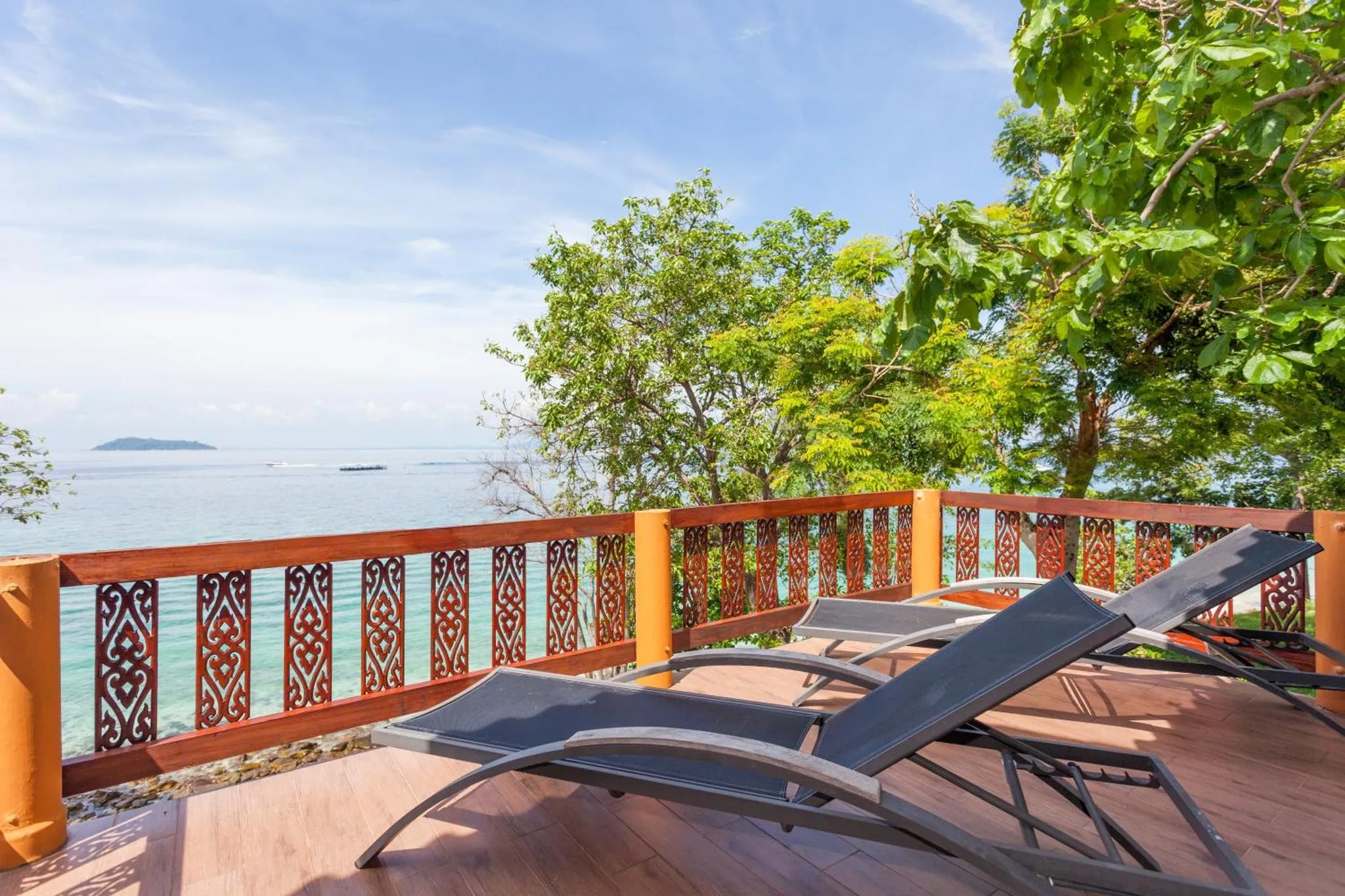 Terrasse en bois avec transats donnant sur la mer et la végétation.