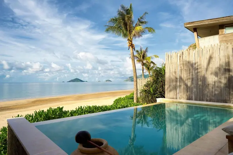 Une piscine à débordement offre une vue sur une plage de sable fin et la mer.