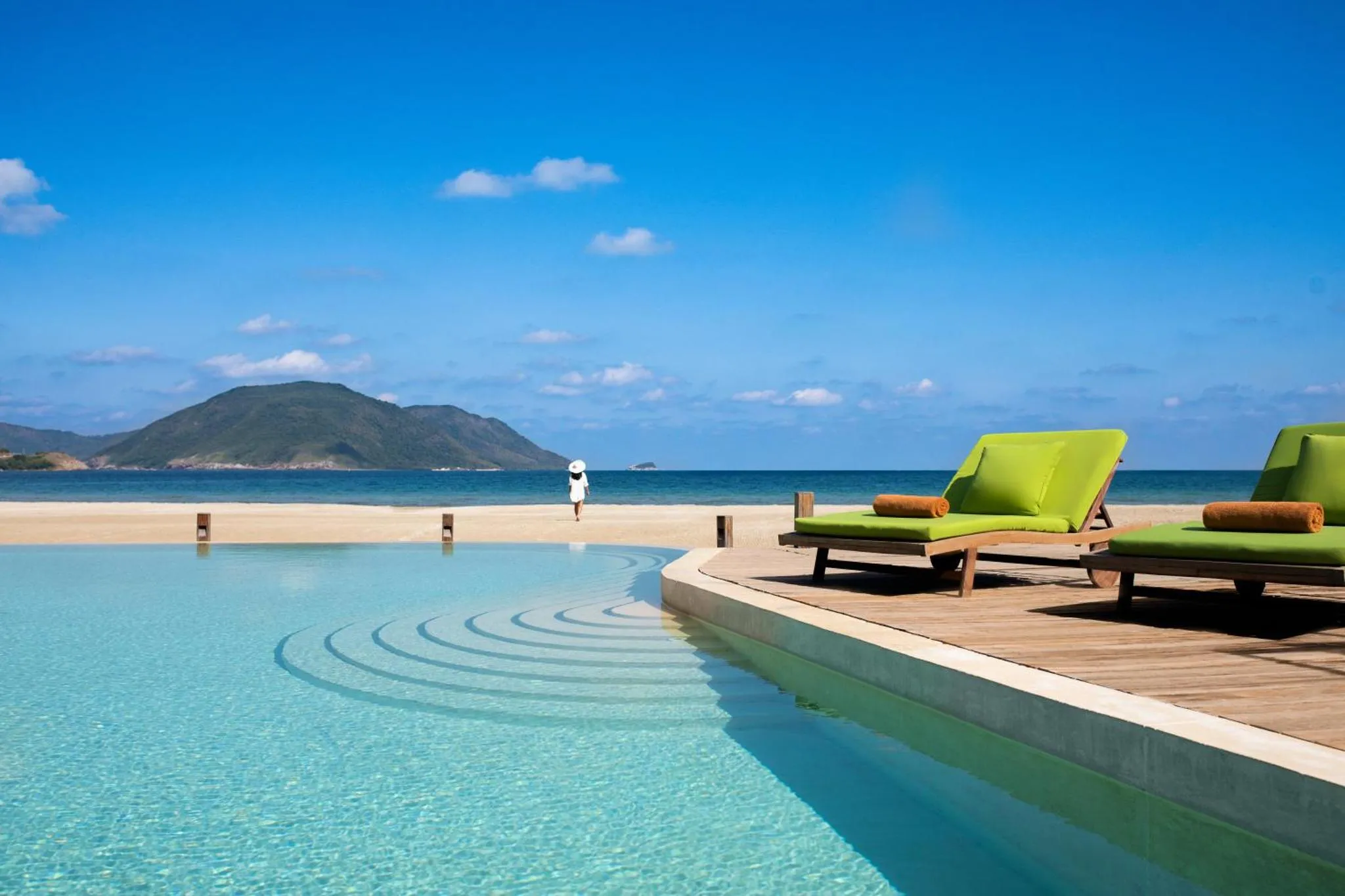 Transats verts au bord d'une piscine turquoise avec vue sur la mer.