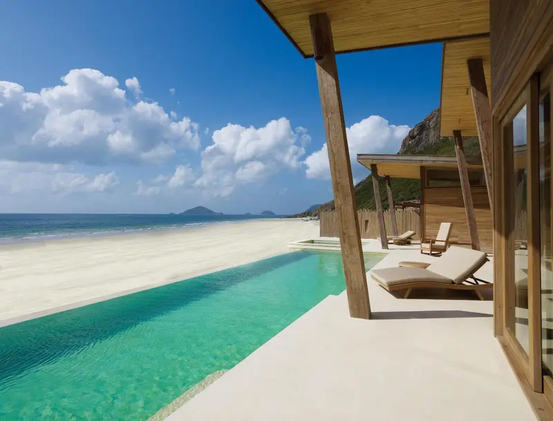 Une piscine à débordement offre une vue sur une plage de sable blanc et une mer turquoise.