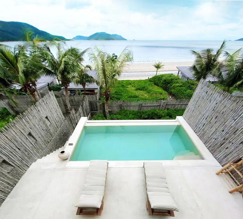 Une piscine rectangulaire est entourée de chaises longues sur une terrasse ensoleillée avec vue sur la mer.