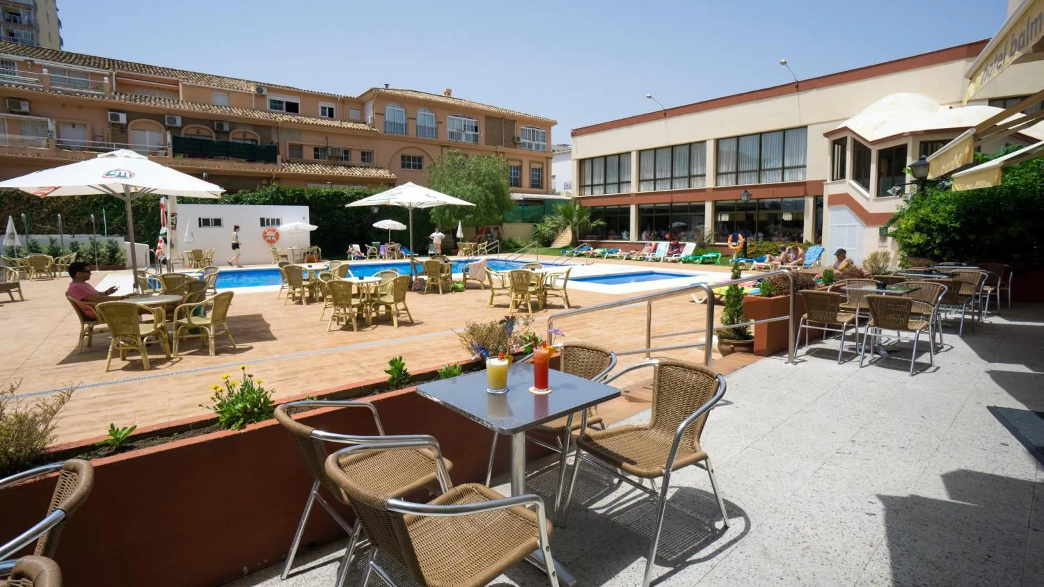 Terrasse avec tables et chaises près d'une piscine ensoleillée.