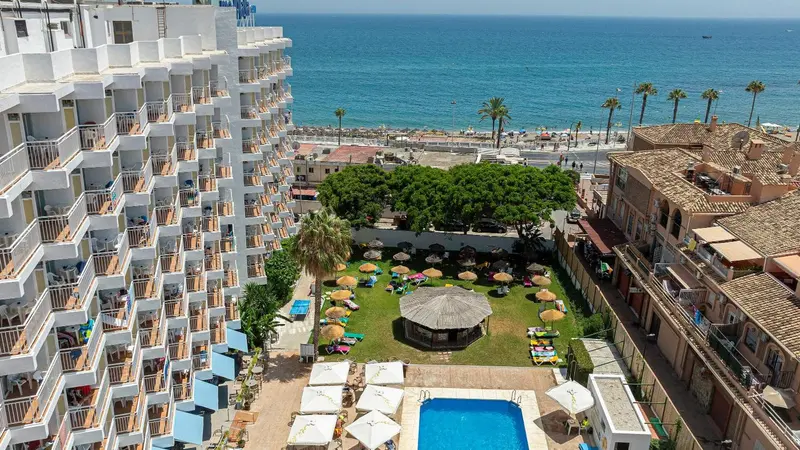 Vue aérienne d'un complexe hôtelier blanc avec piscine et jardin verdoyant face à la mer.