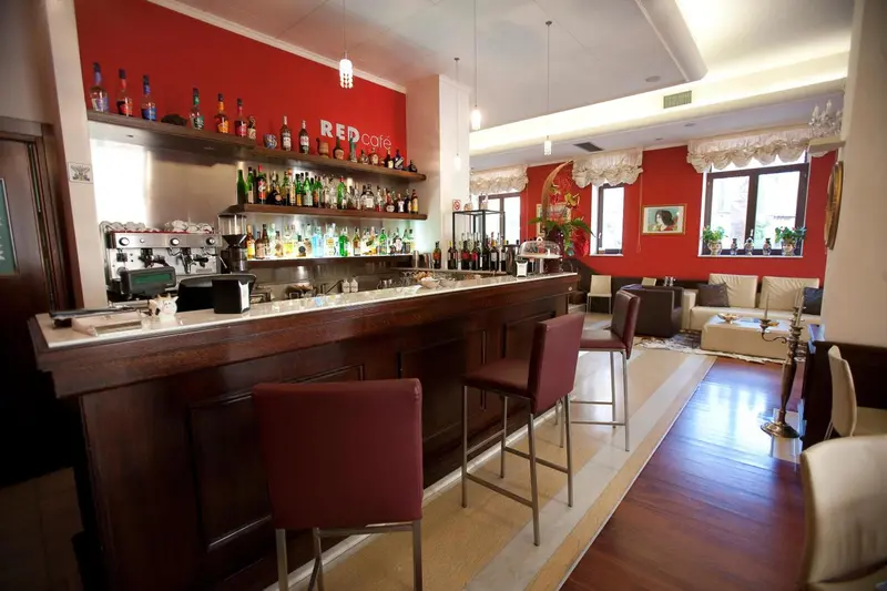 Un comptoir de bar en bois avec des tabourets, devant un mur rouge décoré.