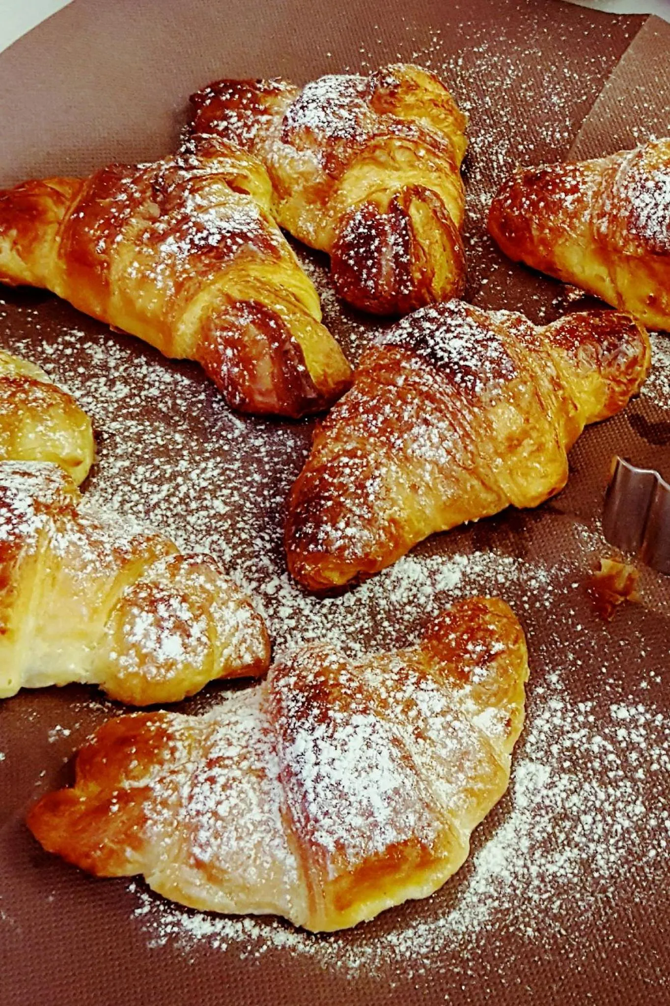 Des croissants saupoudrés de sucre glace sont présentés sur une surface sombre.