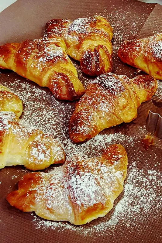 Des croissants saupoudrés de sucre glace sont présentés sur une surface sombre.