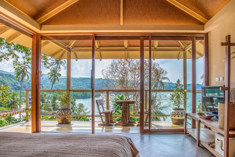 Une chambre lumineuse s'ouvre sur une terrasse avec vue sur la végétation et la mer.