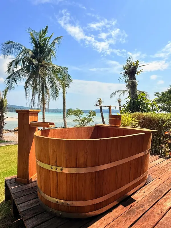 Baignoire en bois sur une terrasse avec vue sur la mer et la végétation.
