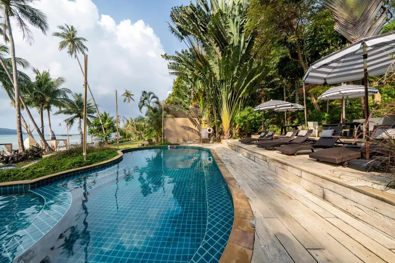 Une piscine bleue bordée d'une terrasse en bois avec des transats à l'ombre de parasols.