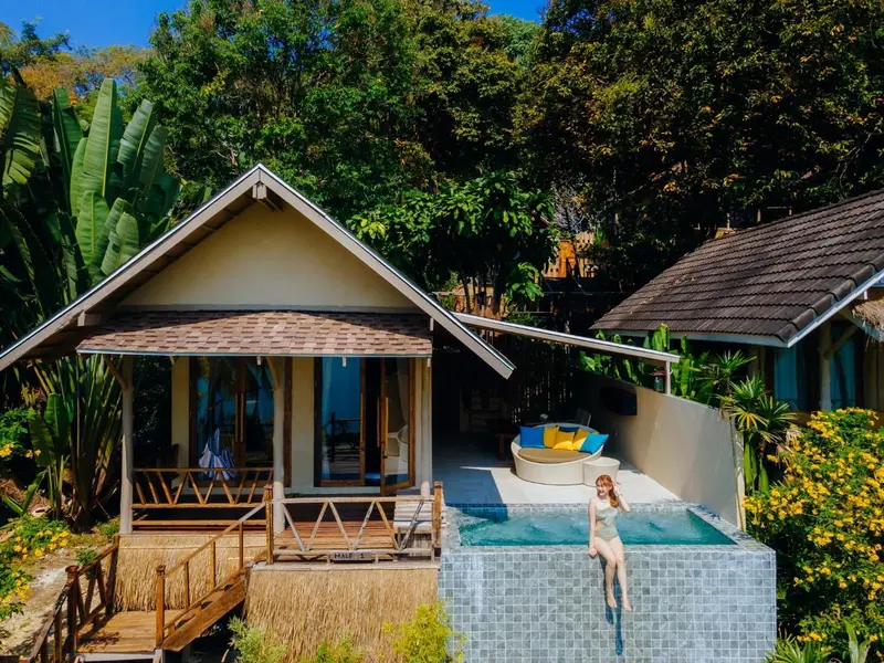 Une personne assise au bord d'une piscine devant un bungalow.