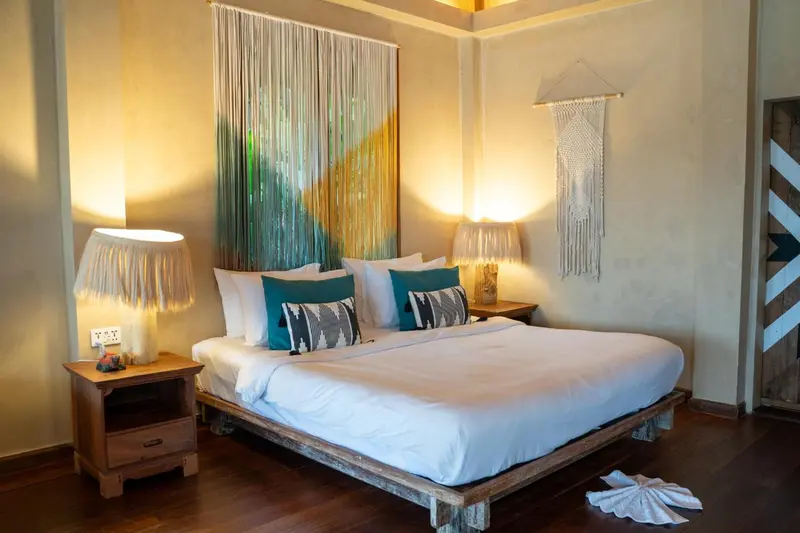 Une chambre lumineuse avec un grand lit recouvert de draps blancs et de coussins turquoise.