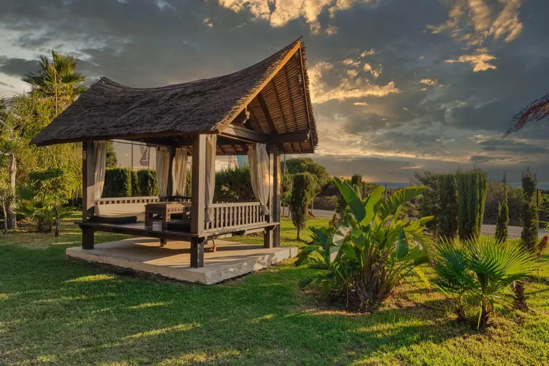 Un pavillon de bois sur une pelouse verdoyante au coucher du soleil.
