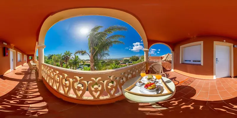 Une table avec un petit-déjeuner est placée sur une terrasse ensoleillée avec vue sur un paysage tropical.