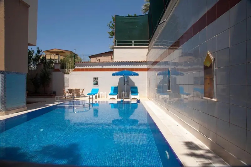 Une piscine rectangulaire bleue avec des transats bleus et un parasol.