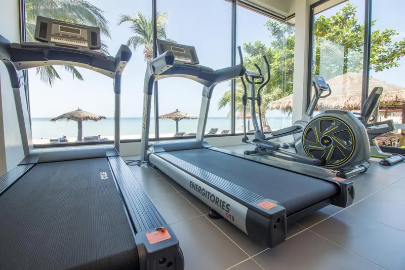 Une salle de sport lumineuse avec des équipements de cardio face à une vue sur la plage.