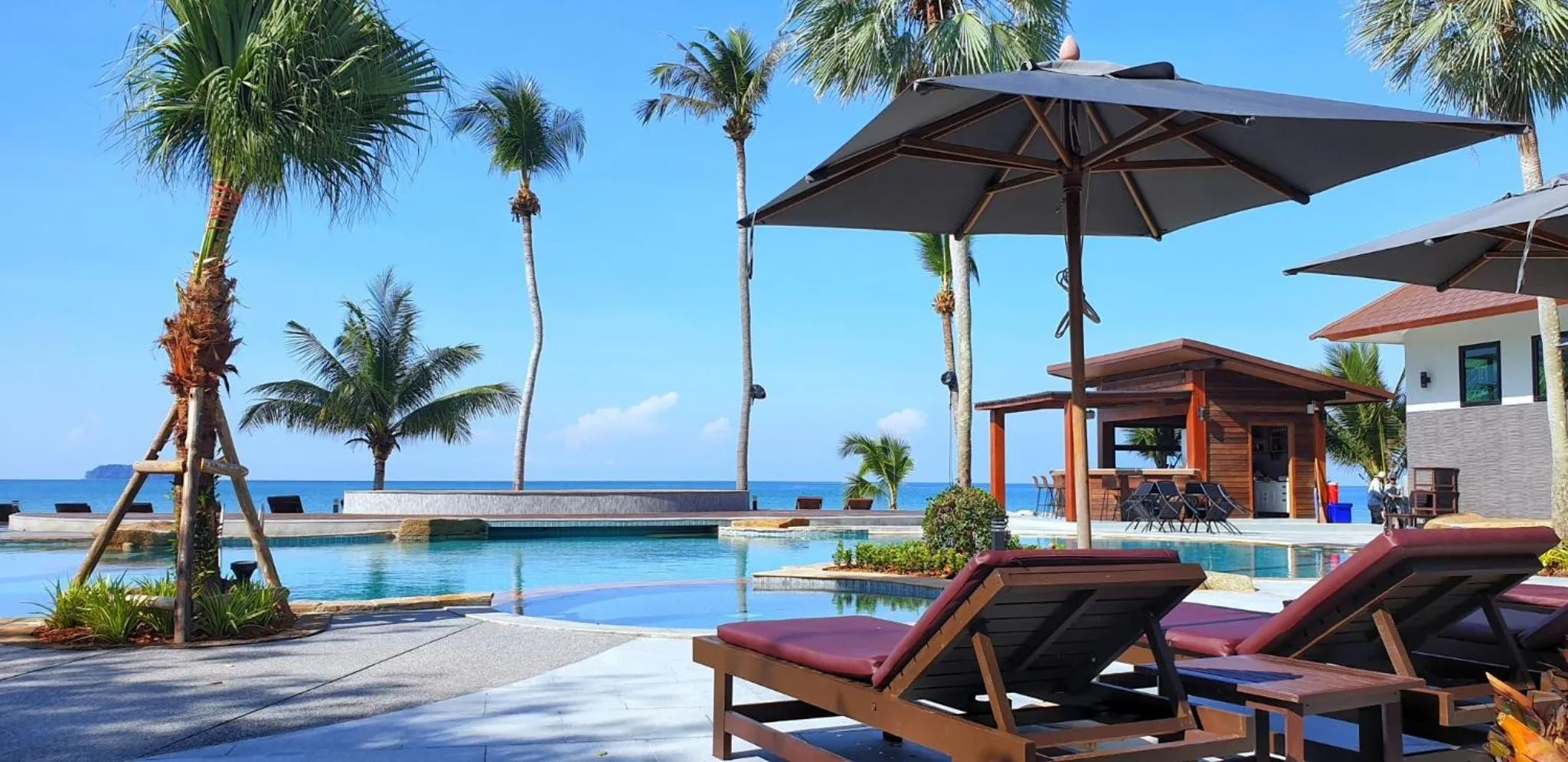 Transats en bois disposés au bord d'une piscine avec vue sur la mer et des palmiers.