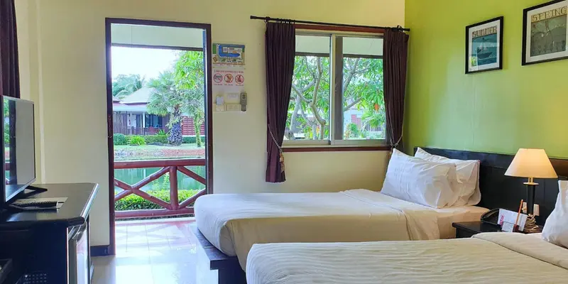 Chambre lumineuse avec deux lits simples et vue sur un jardin tropical.
