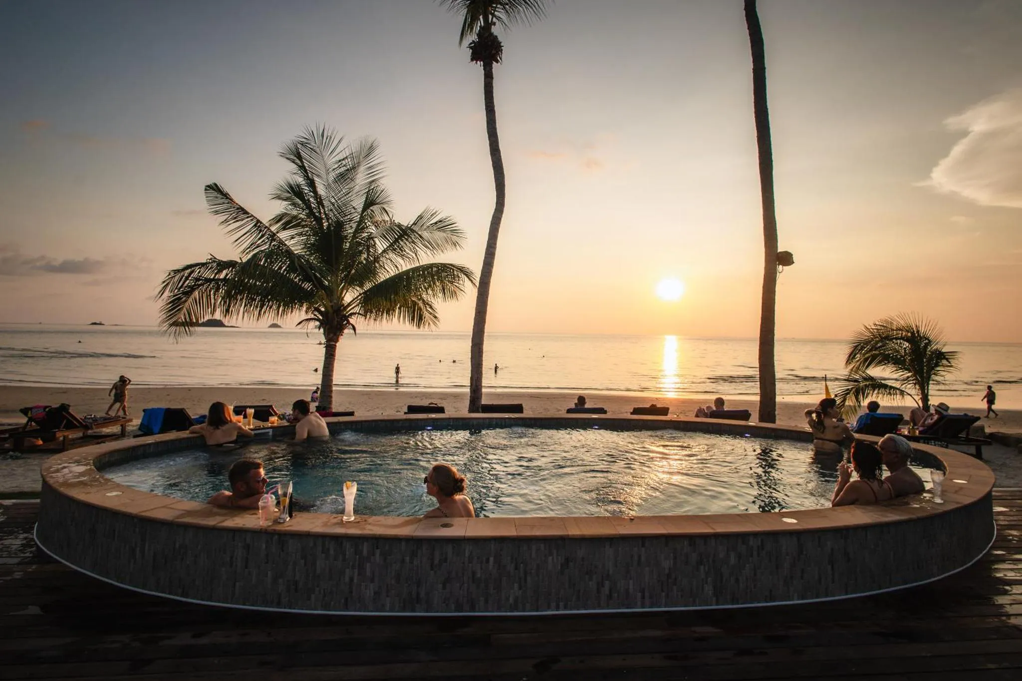 Des personnes se détendent dans un jacuzzi en bord de mer au coucher du soleil.