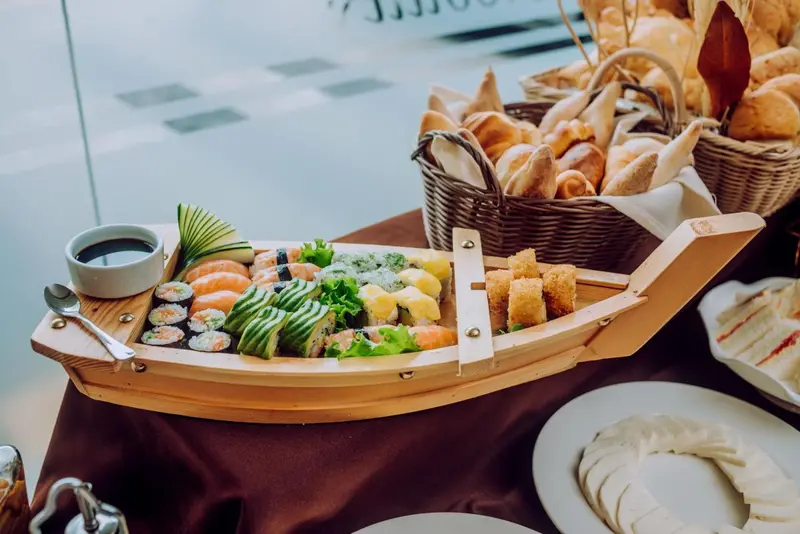 Assortiment de sushis et de beignets présentés dans un bateau en bois sur une table.