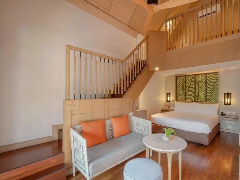 Espace de vie intérieur avec canapé, lit et escalier montant à une mezzanine.