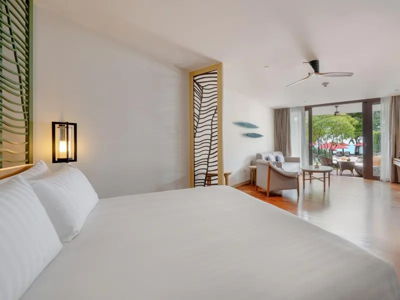 Une chambre lumineuse avec un grand lit et un espace salon ouvert sur l'extérieur.