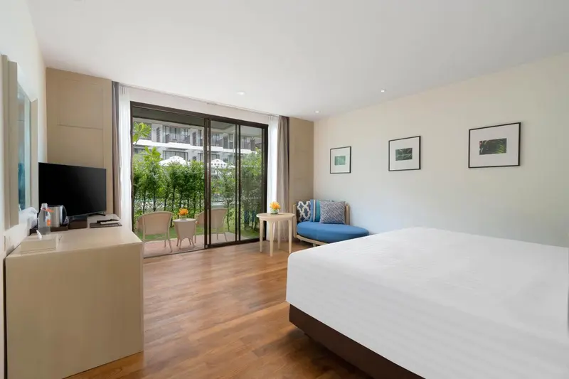 Une chambre lumineuse avec un lit et un coin salon donnant sur une terrasse.