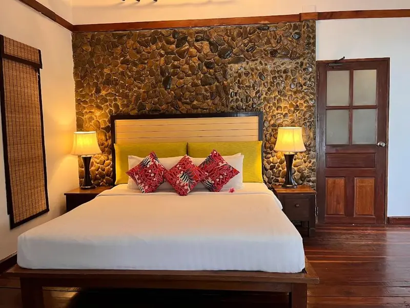 Une chambre lumineuse avec un grand lit recouvert de draps blancs et de coussins colorés.