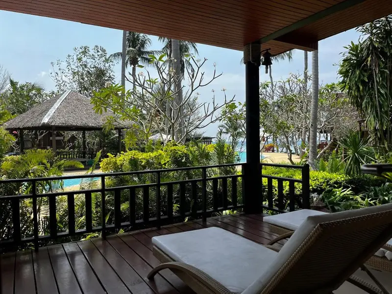 Terrasse en bois avec transats donnant sur une végétation luxuriante et la mer.
