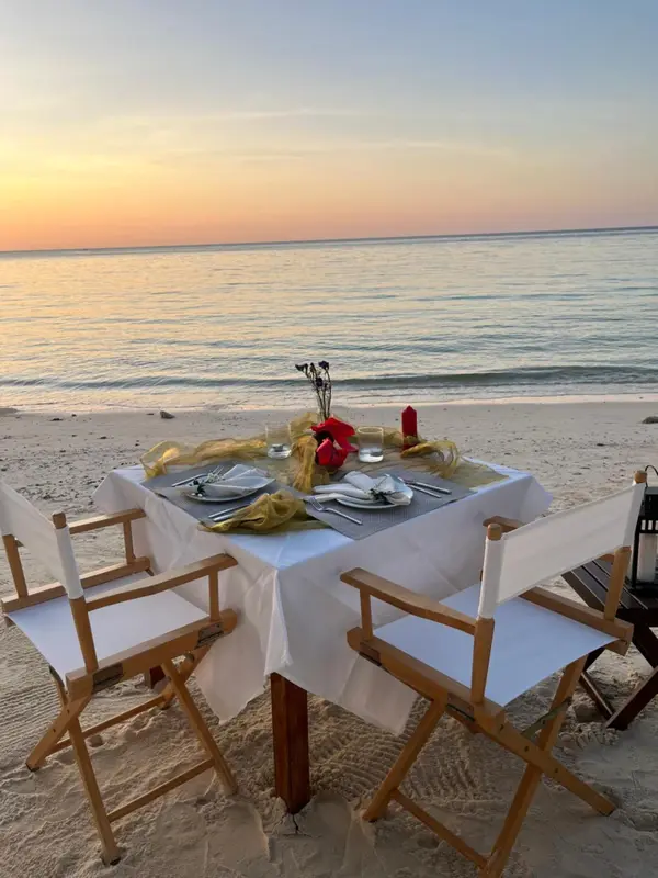 Une table dressée pour deux sur une plage de sable au coucher du soleil.