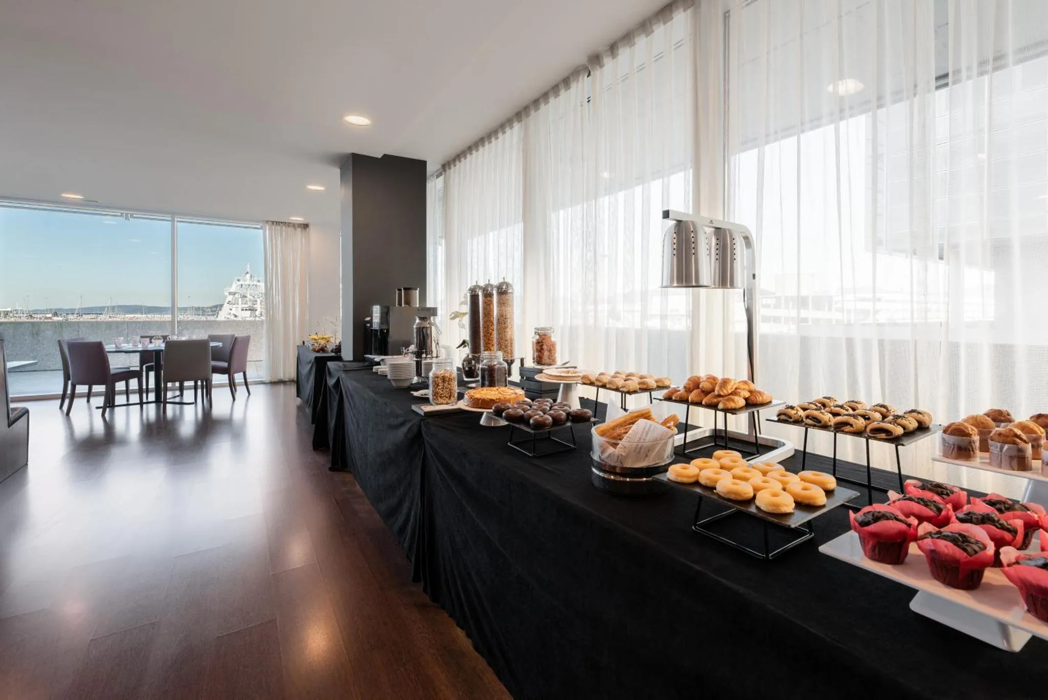 Une table garnie de viennoiseries et de boissons en libre-service dans une salle lumineuse.