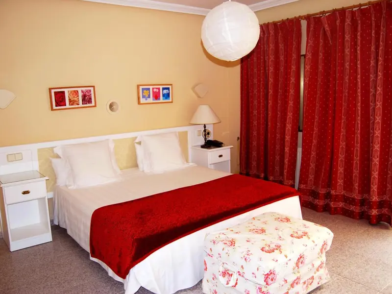 Une chambre lumineuse avec un lit double et des rideaux rouges.