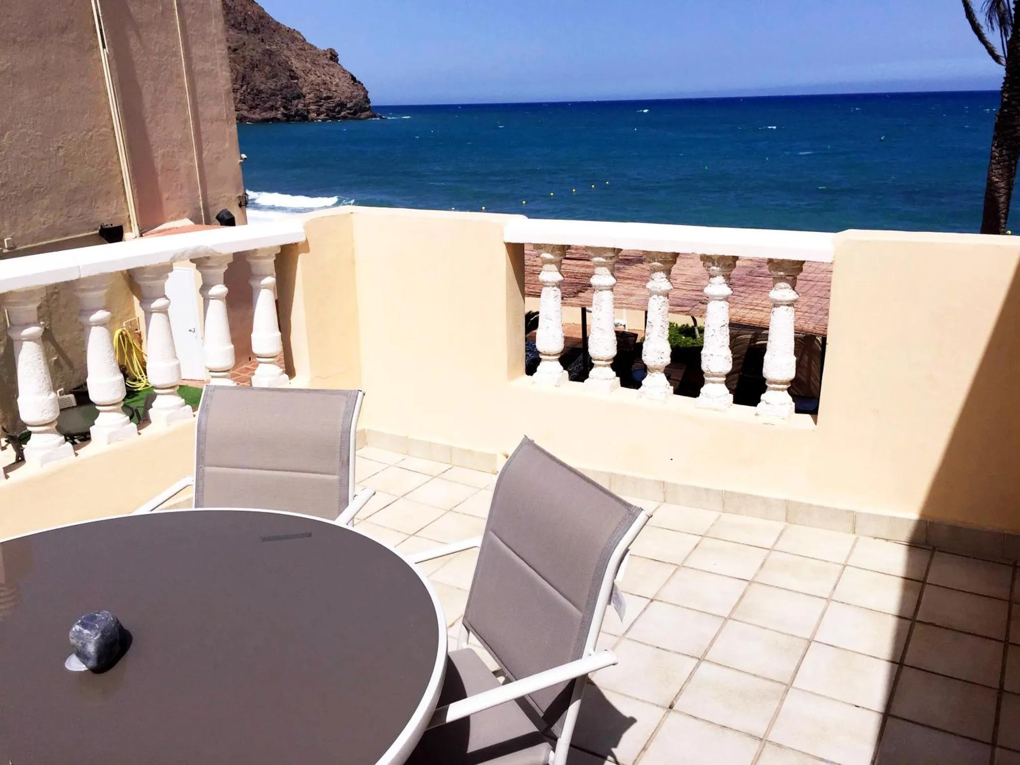 Terrasse carrelée avec table et chaises, vue sur la mer.
