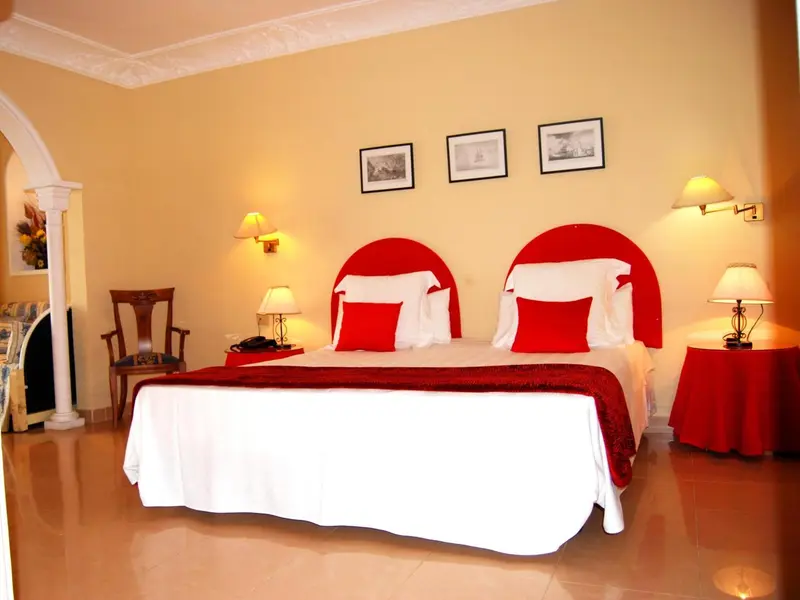 Une chambre lumineuse avec un grand lit recouvert d'une courtepointe rouge et blanche.