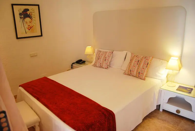 Une chambre lumineuse avec un grand lit recouvert d'une courtepointe rouge.