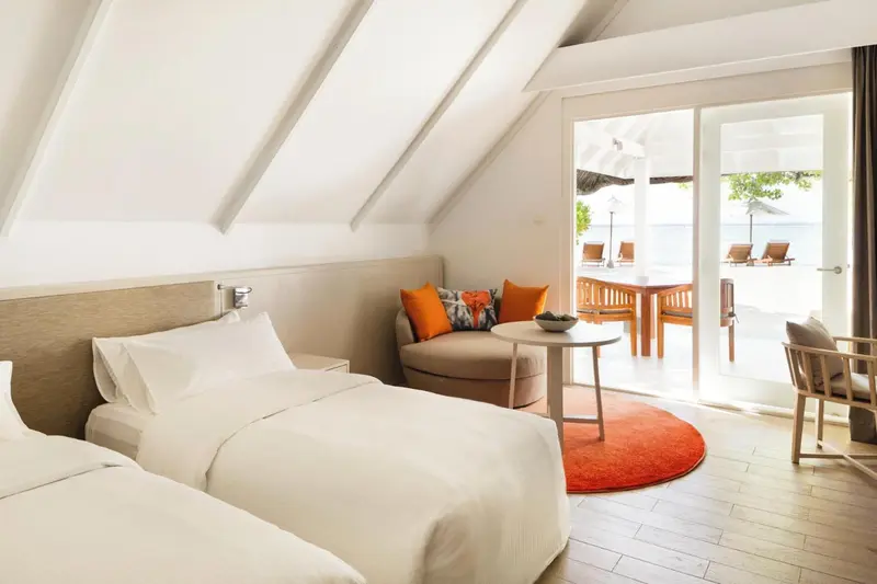 Chambre lumineuse avec un lit blanc et un coin salon donnant sur une terrasse.