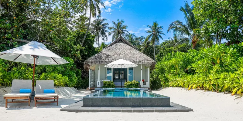 Une villa avec piscine privée et transats sur une plage de sable blanc.