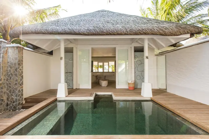 Petite piscine devant une villa au toit de chaume.