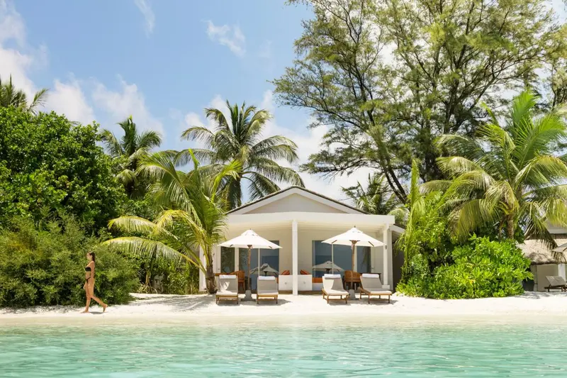 Une plage de sable blanc bordée de palmiers et d'une maison au toit clair.