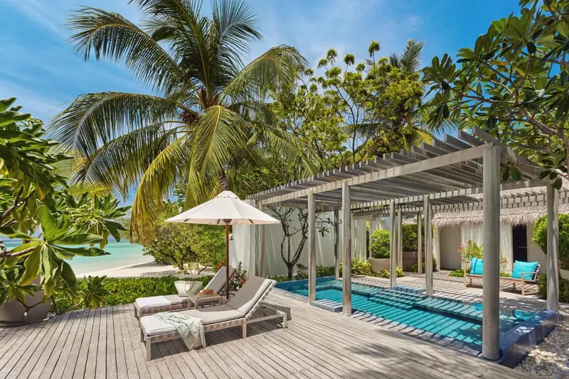 Terrasse en bois avec transats et piscine turquoise bordée de végétation.