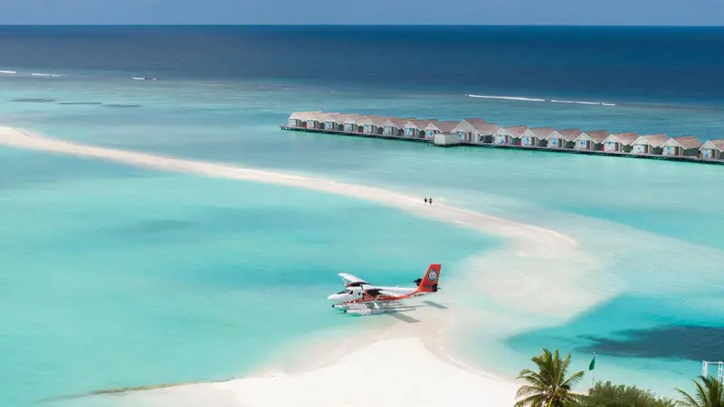 Vue aérienne d'un atoll avec des bungalows sur pilotis et un hydravion sur une plage.