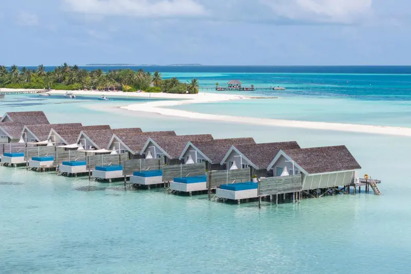 Vue aérienne d'une série de bungalows sur pilotis au-dessus d'un lagon turquoise.