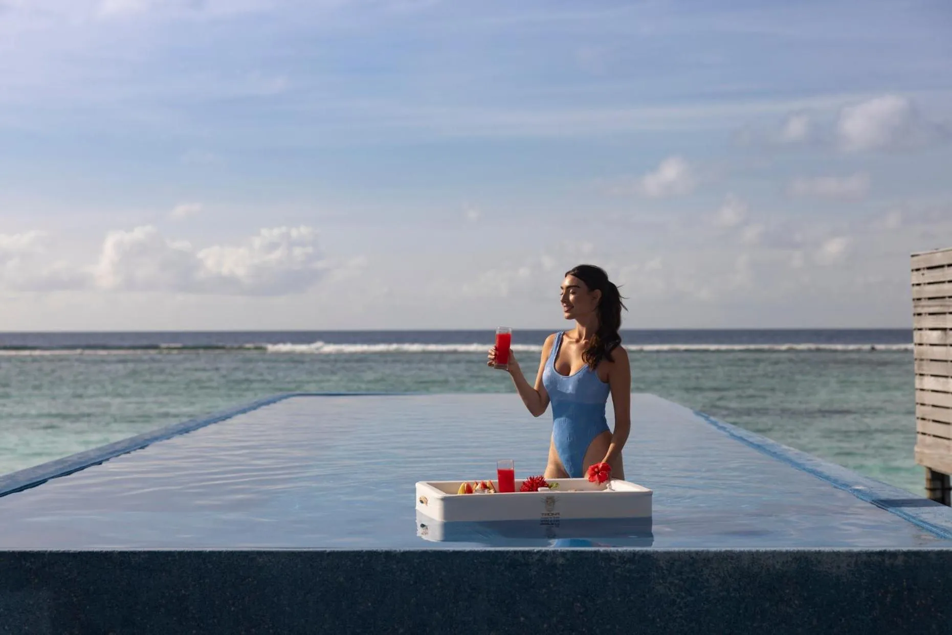 Une femme se tient au bord d'une piscine à débordement avec des boissons.