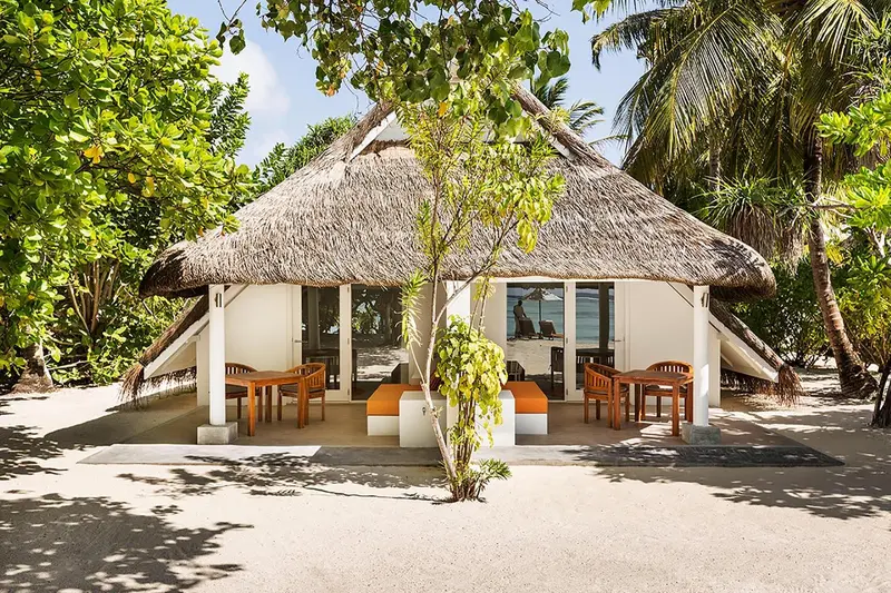 Une maison de plage à toit de chaume avec une terrasse meublée.