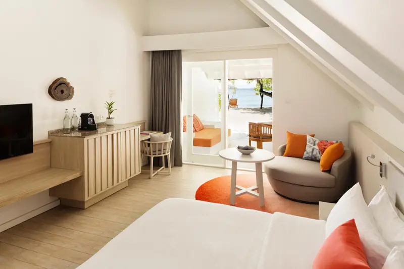 Une chambre lumineuse avec un coin salon donnant sur une plage.