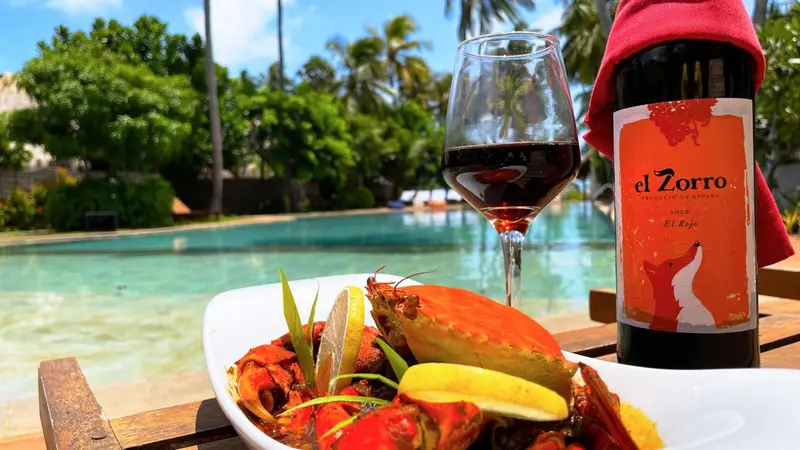 Un verre de vin rouge et un plat de crabe sont servis au bord d'une piscine.