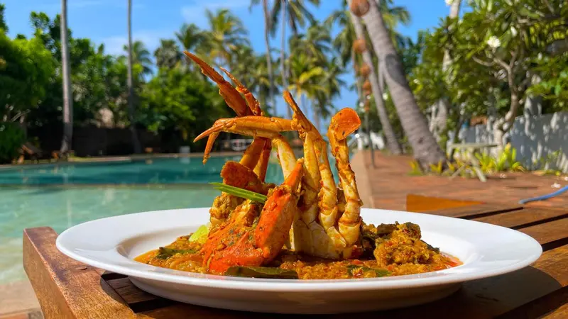 Un plat de crabe épicé est présenté sur une table en bois près d'une piscine.